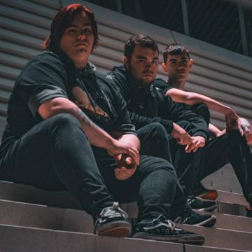 Three people sitting on steps at night, wearing dark clothing, looking towards the camera.