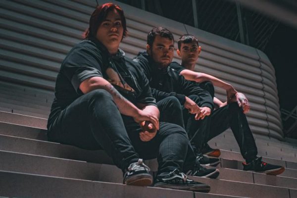 Three people sitting on steps at night, wearing dark clothing, looking towards the camera.