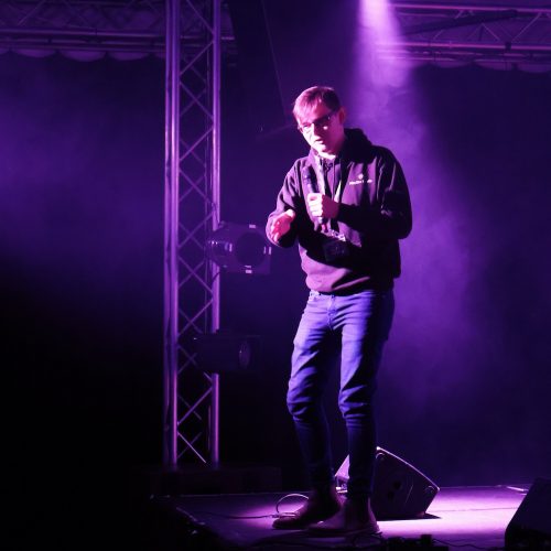 Person talking on stage under purple lighting.