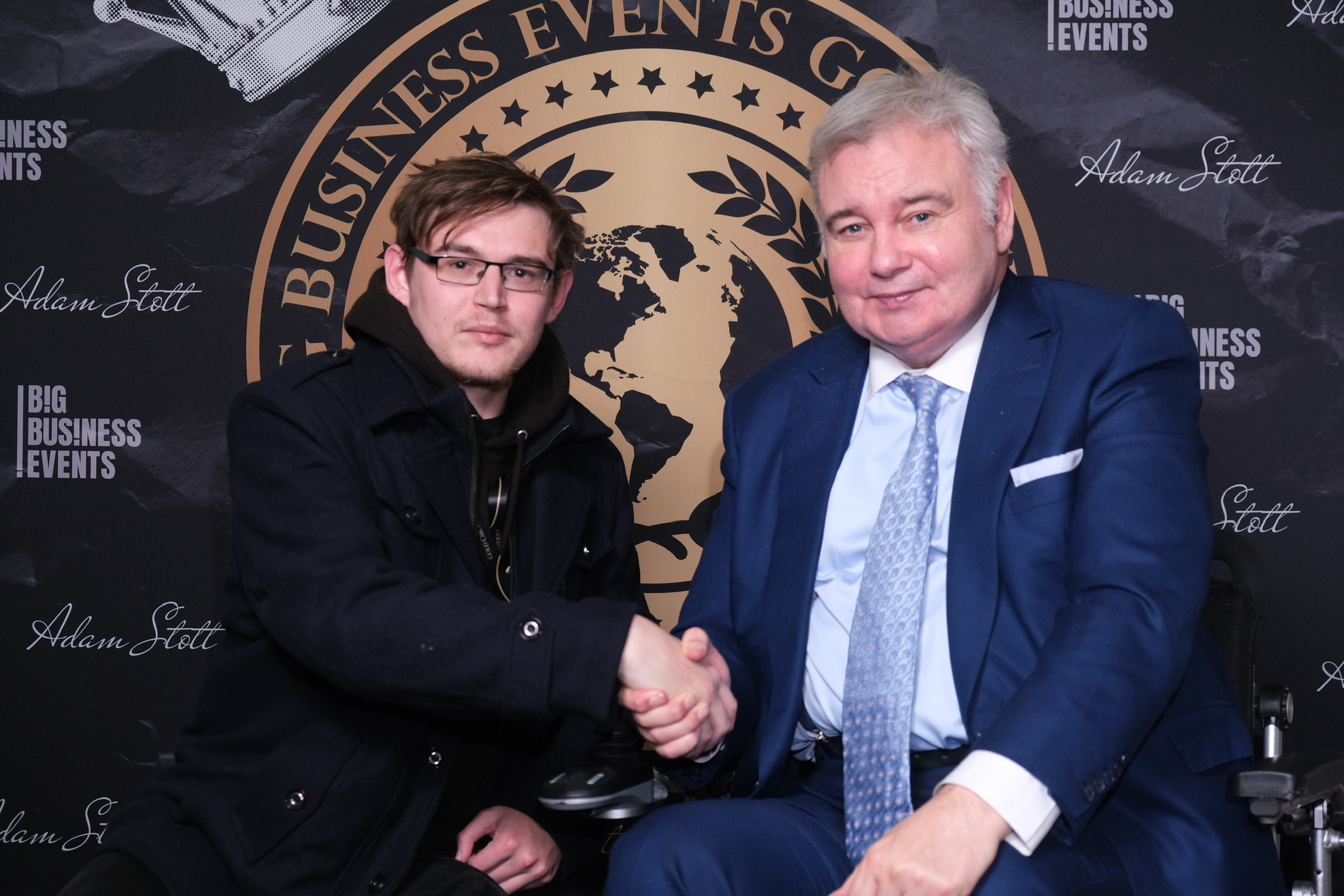 Two men shaking hands in front of a backdrop with logos and text Big Business Events and Adam Stott.