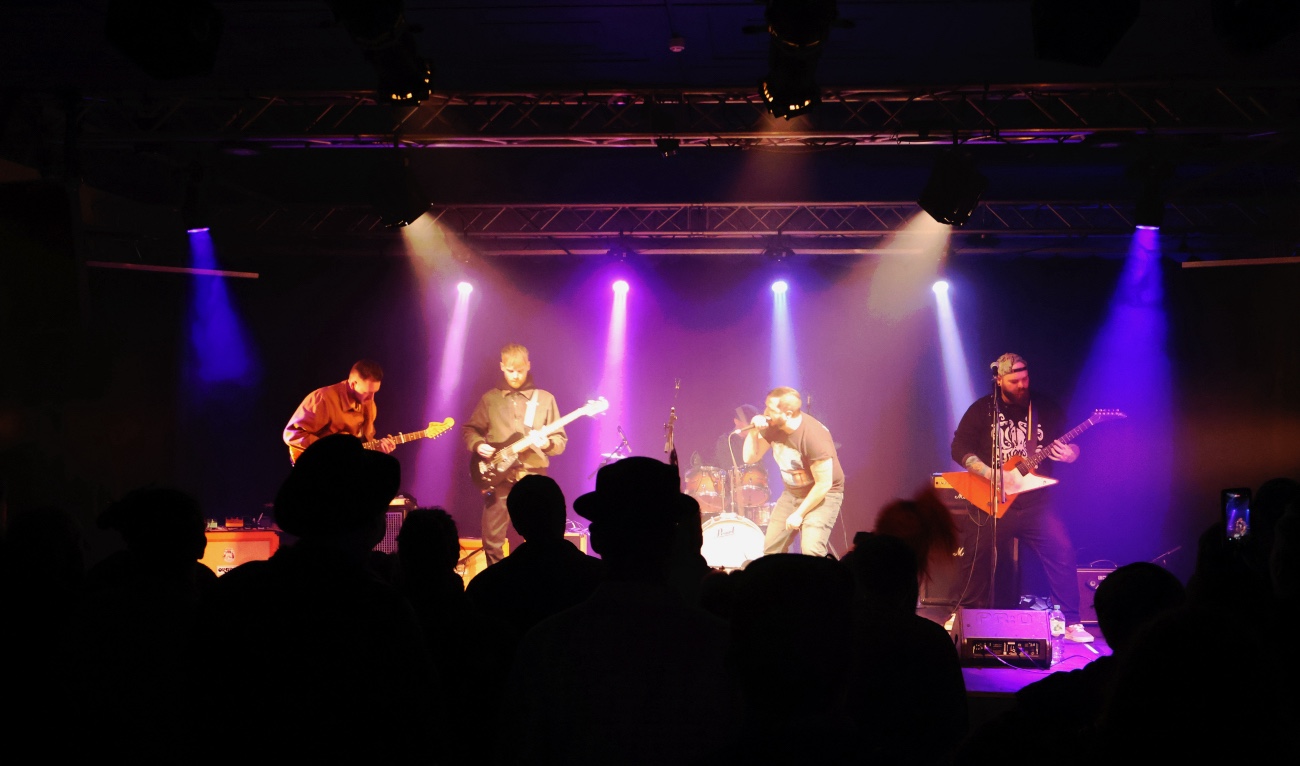 Band performing on stage with colorful lights; audience silhouettes in the foreground.