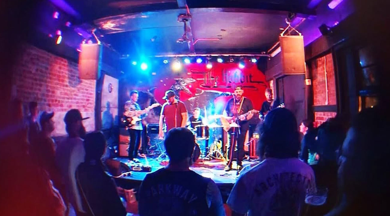 Band performing on stage with colorful lights and audience watching in a dimly lit venue.